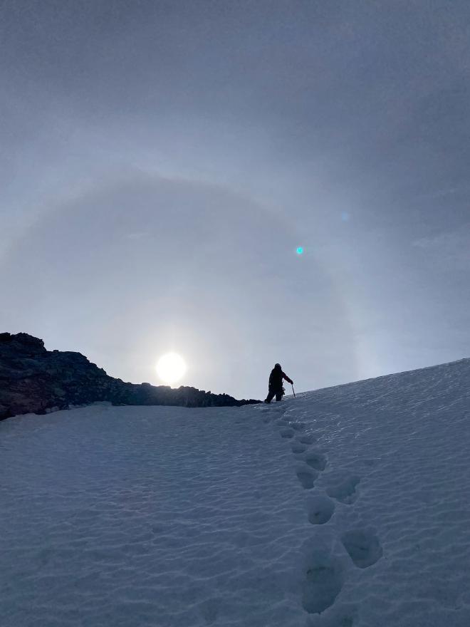 Climbing the snow as the sun comes up, with a faint halo around it