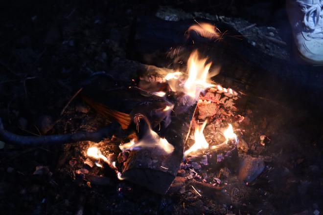 Embers and flame from our campfire at night, someone&rsquo;s shoe just in frame