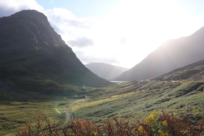 Golden evening light spilling into a glen, mountains rising on either side of the road