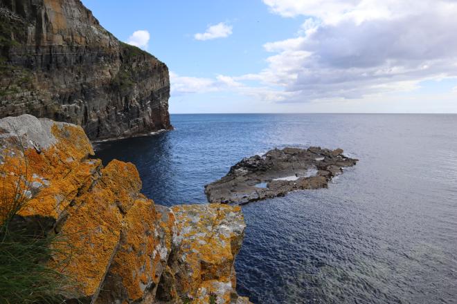 Orange lichen-covered sandstone cliffs framing the sea near Whaligoe