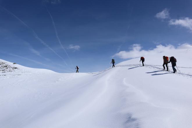 four hikers on open snow field under blue sky