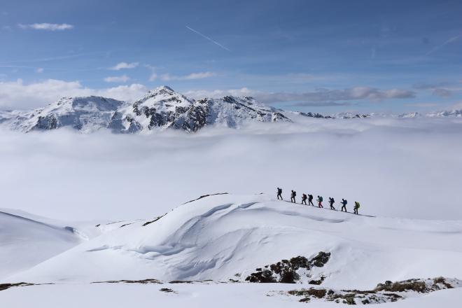 hikers in line on ridgeline above sea of clouds