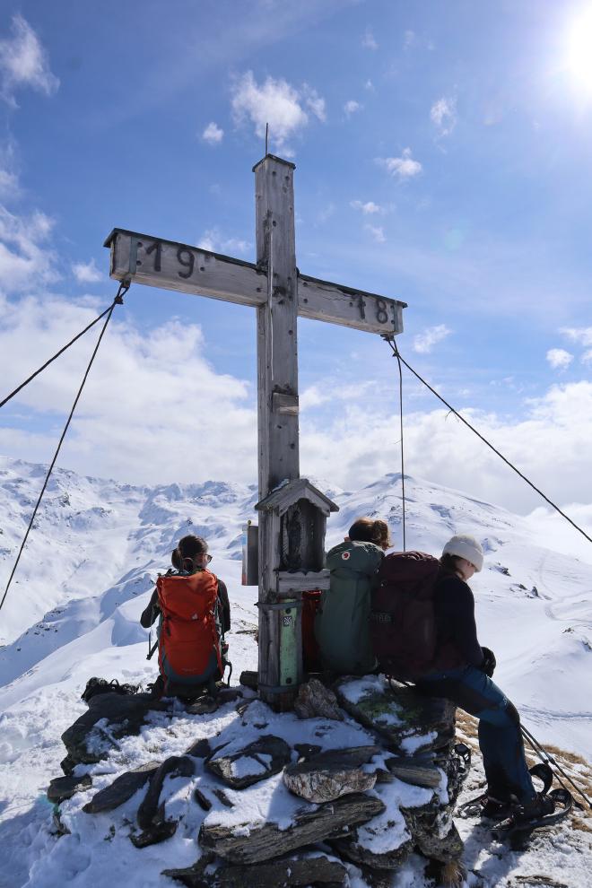 summit cross with two hikers under blue sky